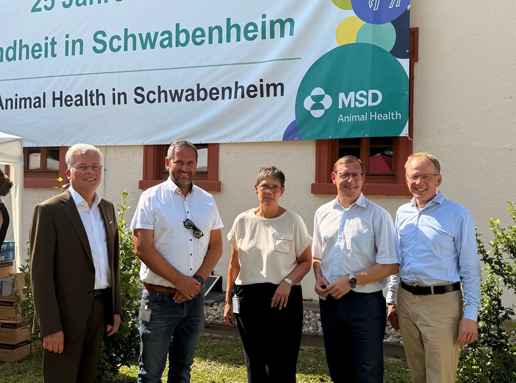 MSD Animal Health Team in Schwabenheim 2 Fünf Personen lächeln vor einem MSD Animal Health Banner in Schwabenheim bei sonnigem Himmel