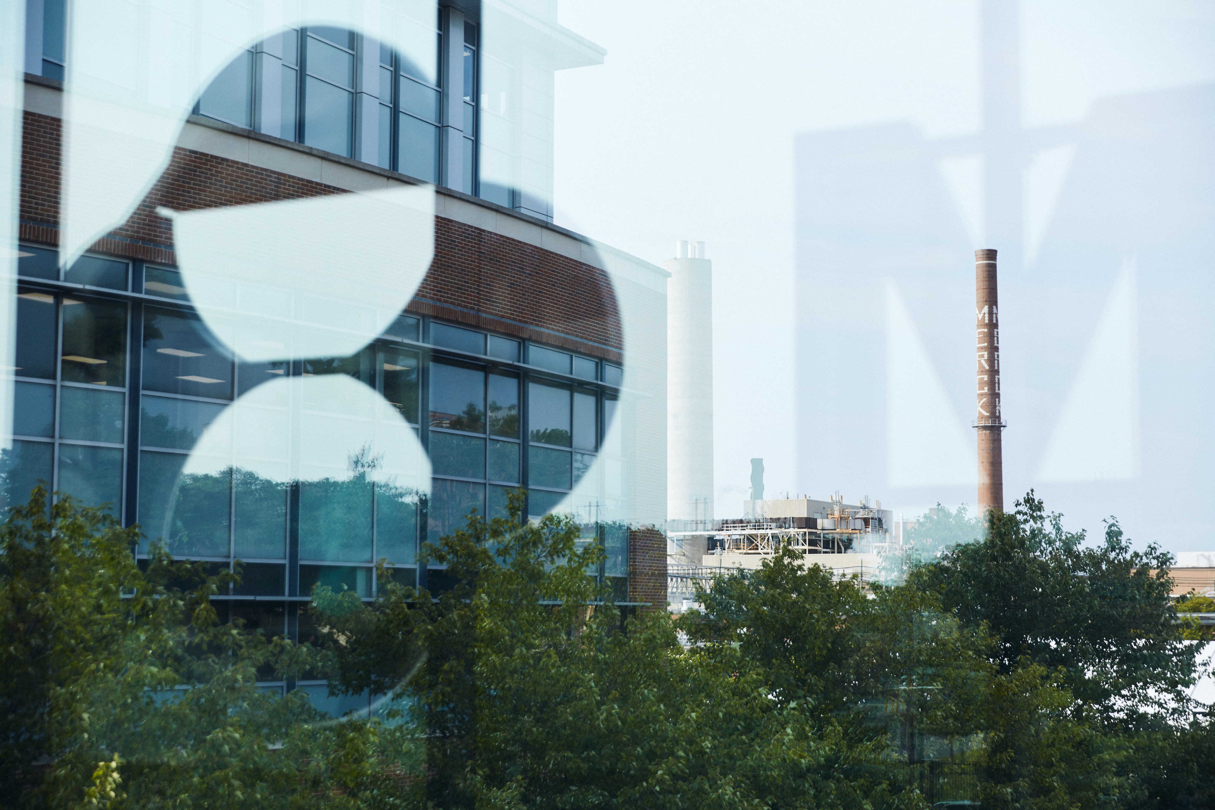 Modernes Campusgebäude Glasbürogebäude mit Bäumen und einem Industrieschornstein in der Ferne.
