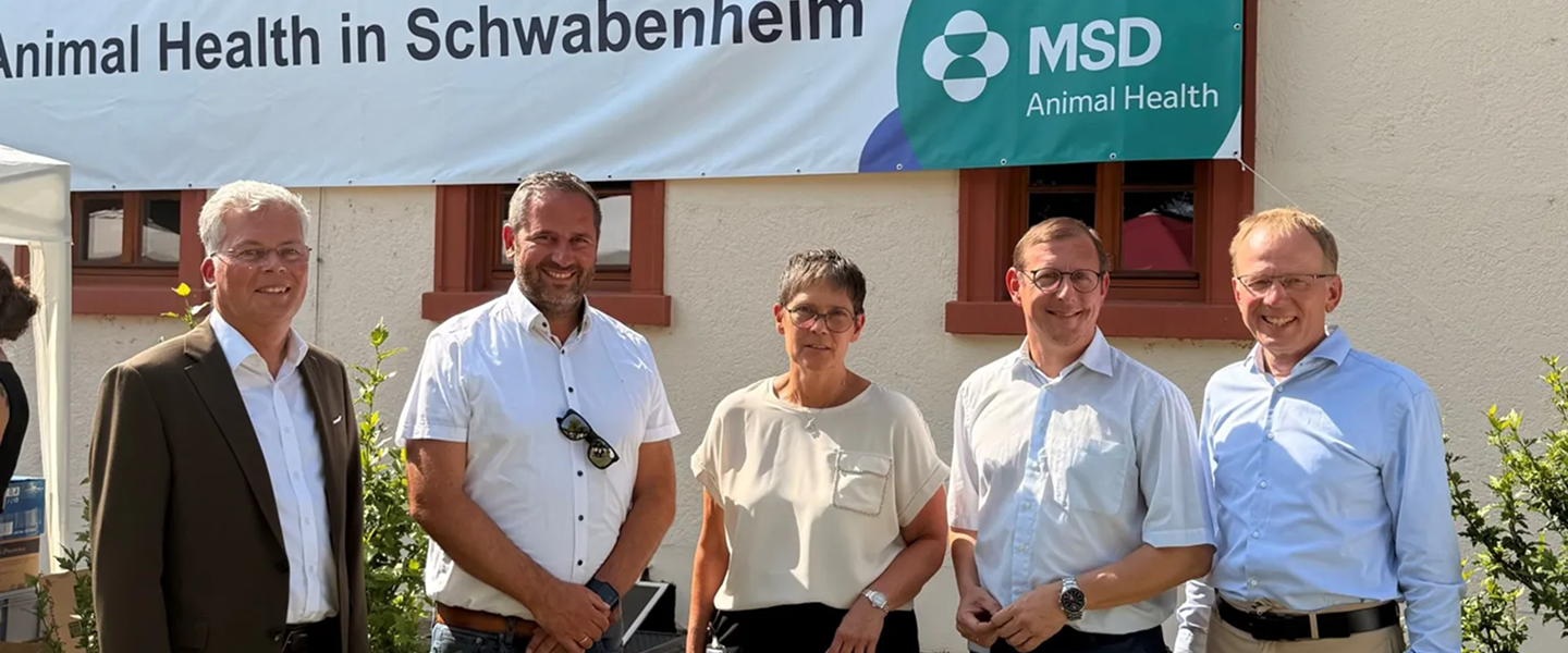 MSD Animal Health Team in Schwabenheim Fünf Personen lächeln vor einem MSD Animal Health Banner in Schwabenheim bei sonnigem Himmel