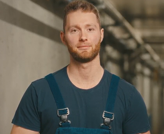Junger Landwirt in Arbeitskleidung Porträt eines jungen Mannes mit Bart in dunkler Arbeitslatzhose.
