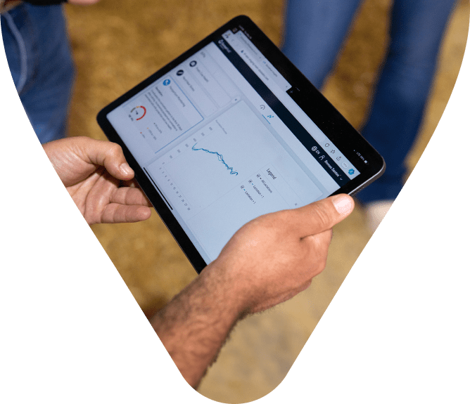 Hände eines Landwirts halten ein Tablet mit einem Analyse-Dashboard für Viehdaten.
