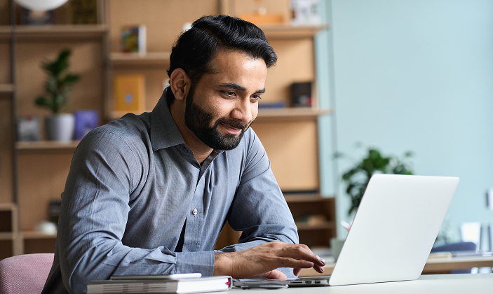 Büroarbeit am Laptop Ein lächelnder Mann mit Bart arbeitet konzentriert an einem Laptop im Büro.